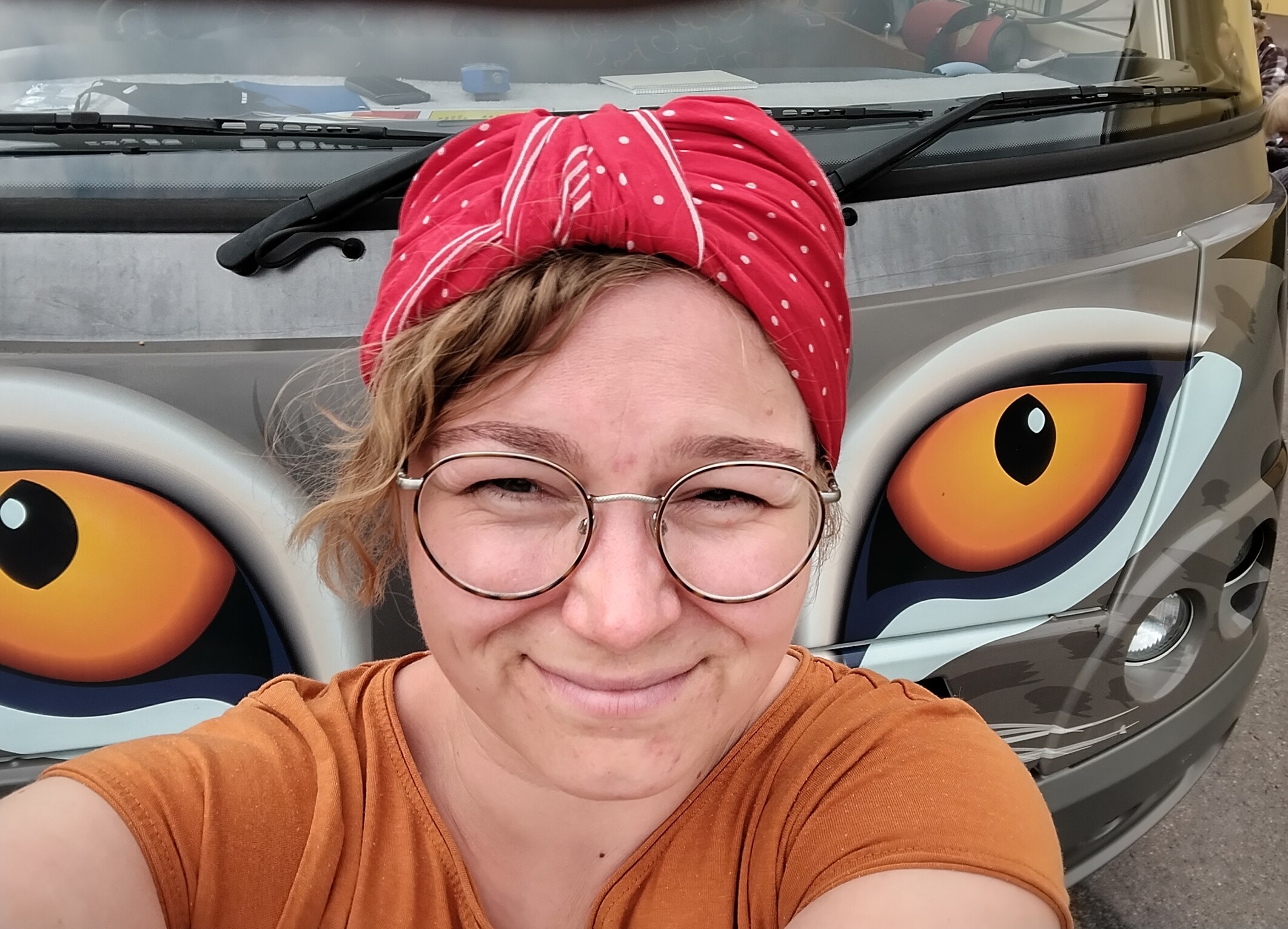 Hymyilevä nainen kissasilmäisen auton edessä ottaa selfien