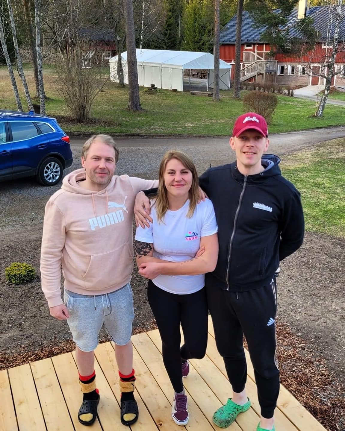 Aseman Lasten työntekijät Jari (Hune) Raikunen sekä projektityöntekijät Miisa Lohi ja Pietro Saari seisovat rinnakkain. Taustalla näkyy sininen auto, puita ja punainen rakennus.