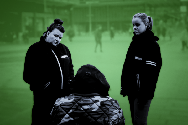 Mustavalkokuva sävytetty vihreällä. Kaksi aikuista juttelevat istumassa olevalle nuorelle