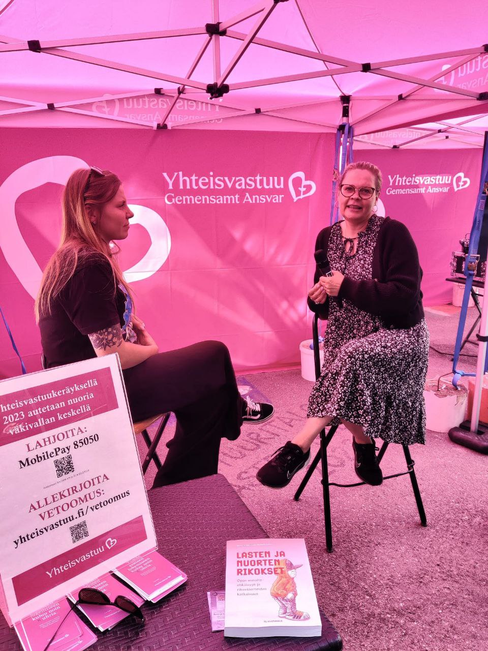 Kaksi naista istuu mikkien kanssa pinkin teltan sisällä haastattelutilanteessa.