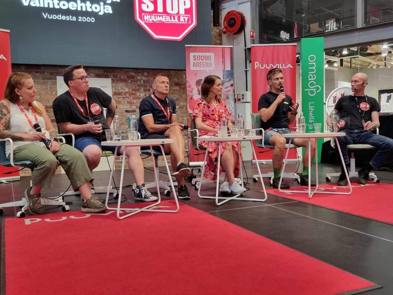 Kuusi ihmistä istuu lavalla rivissä panelisteina.