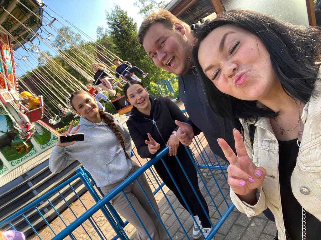Kaksi aikuista ja kaksi nuorta selfiekuvassa hymyilemässä ja virnuilemassa huvipuiston keinukarusellin edessä.
